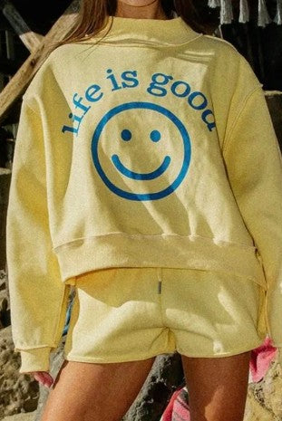 Person wearing a yellow 'Life is Good' sweatshirt with a smiley face graphic.