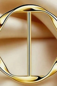 A gold-toned metal belt buckle with a twisted circular design and a central vertical bar, shown on a soft beige satin background.