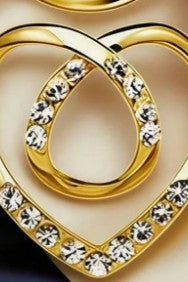 Gold heart-shaped ring with clear rhinestones, shown in a close-up product shot on a beige and dark navy background.