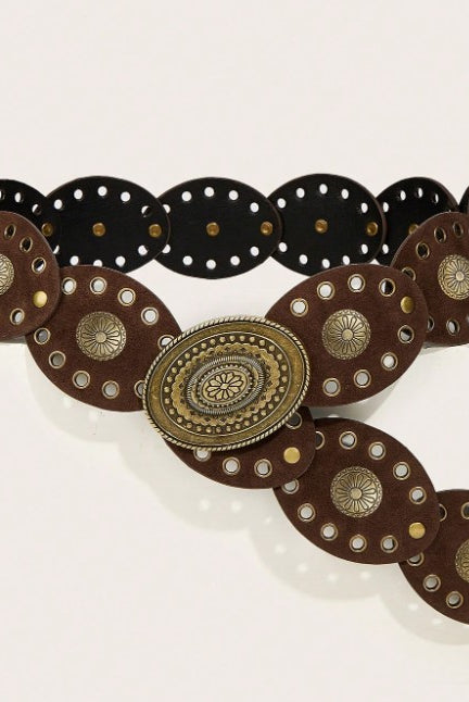 A western-style belt with dark brown leather panels, silver-tone metal studs, and a large ornate oval buckle in an antique gold/bronze finish, displayed on a light beige background.