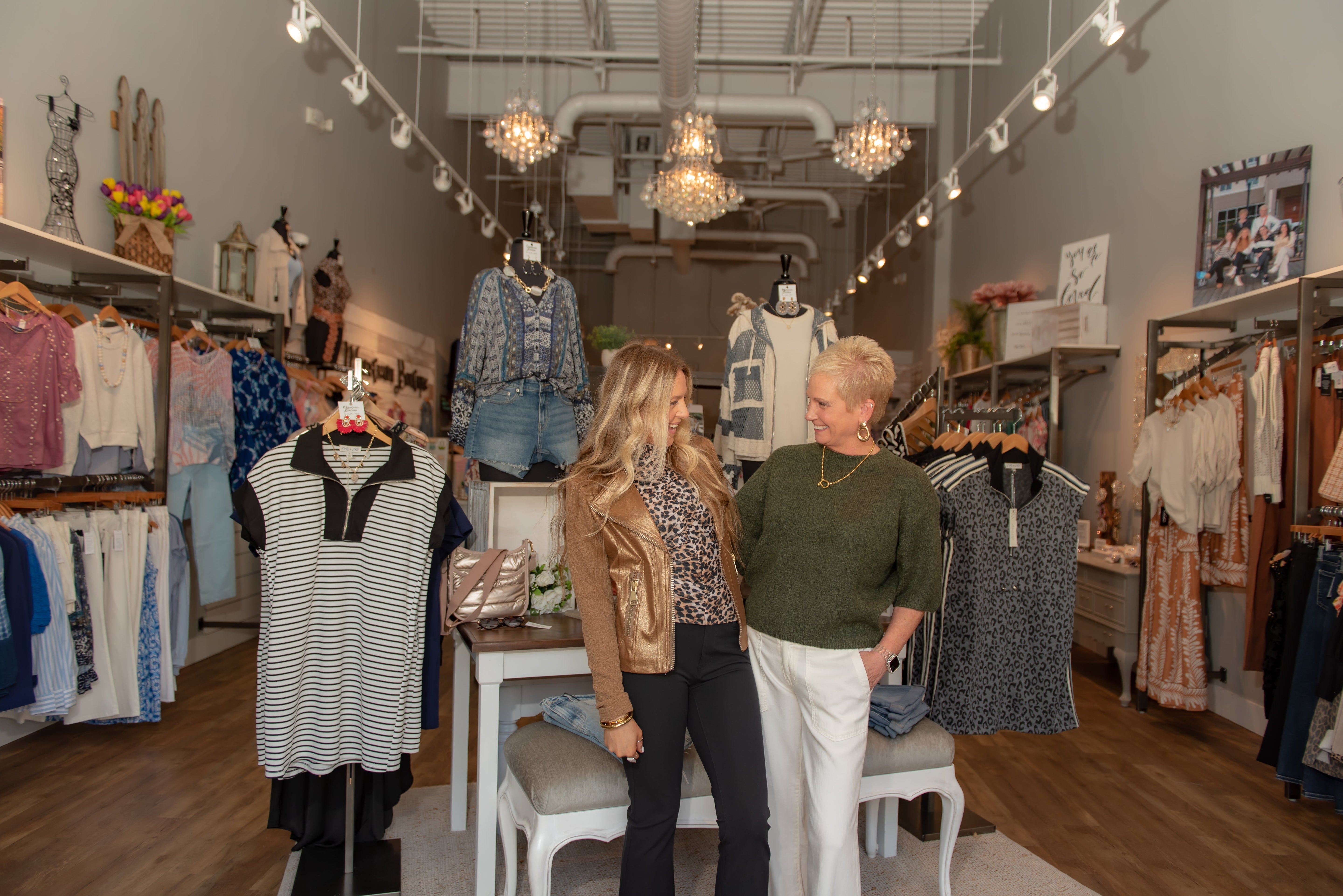 A high quality image of two women standing in a boutique full of summer and early fall fashions smiling and modeling clothes from Mainstream Boutique Charlotte