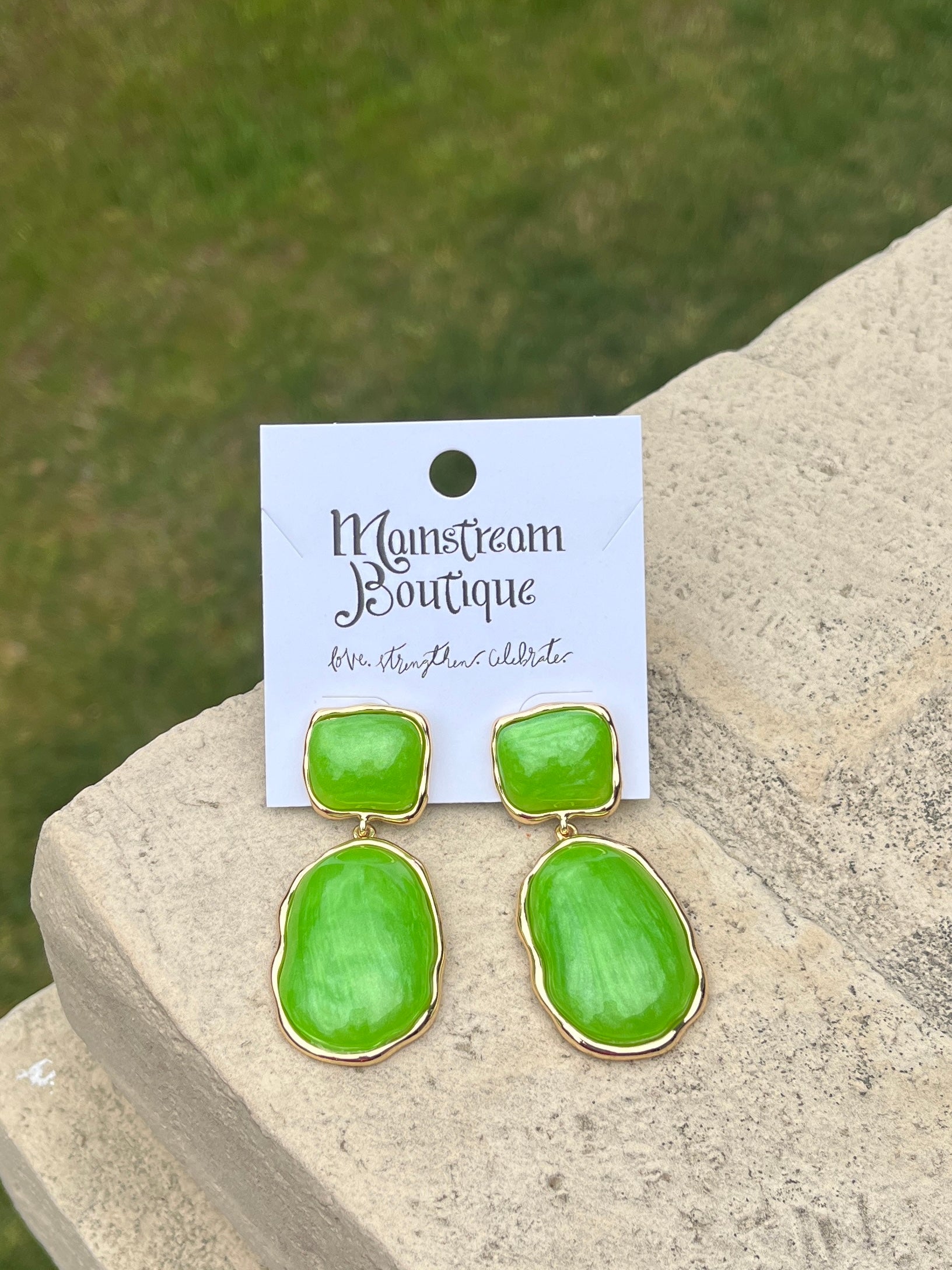 Green earrings placed on a stone surface.