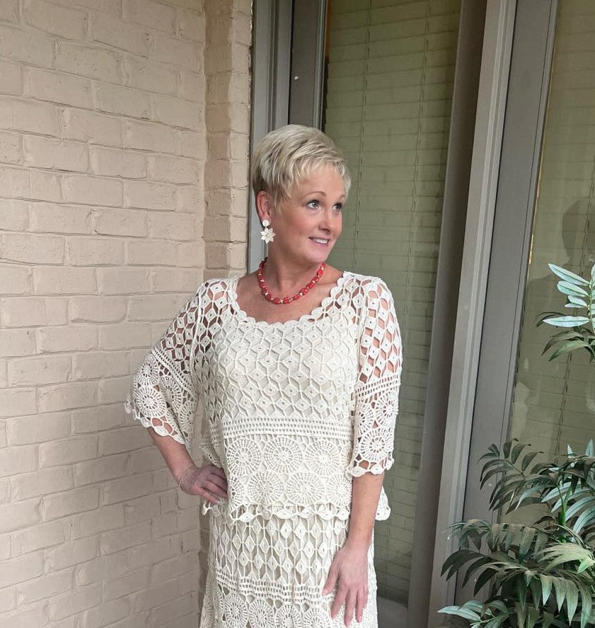 Woman wearing a white lace dress standing against a beige brick wall.