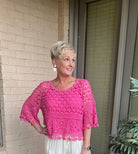 Woman wearing a pink crochet top standing outside a building.