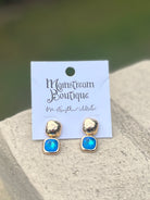 Gold and piercing blue earrings placed on a stone surface.