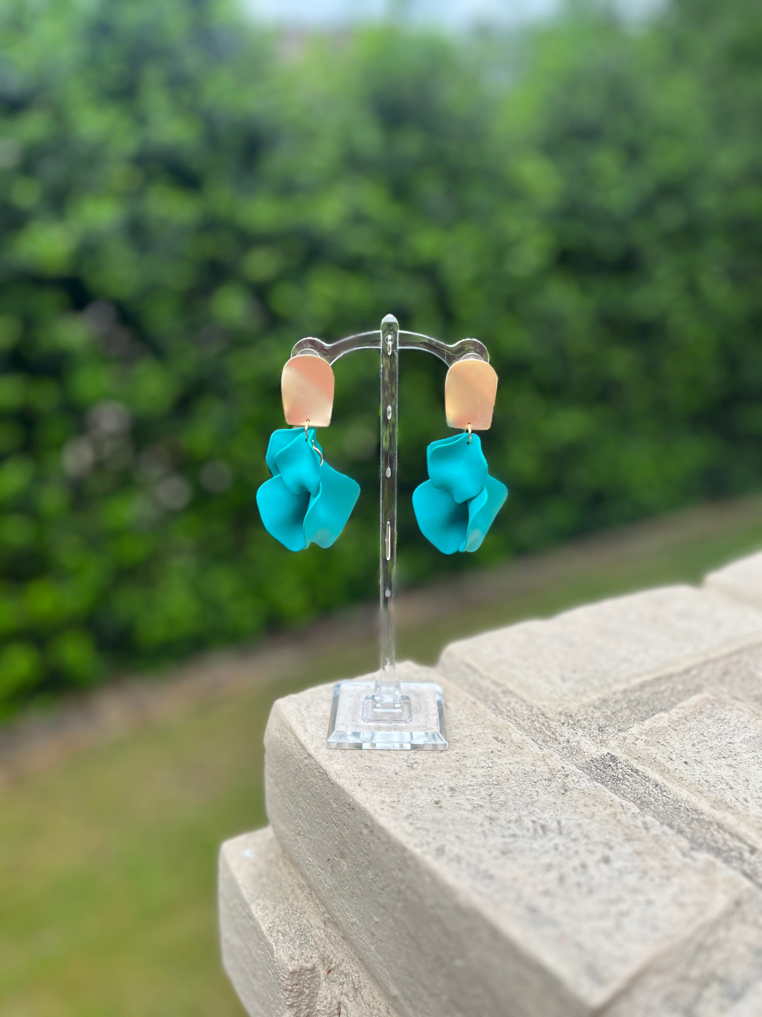 Turquoise flower-shaped earrings on a stand with a blurred green background