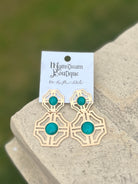 Gold earrings with turquoise stones placed on a stone surface.