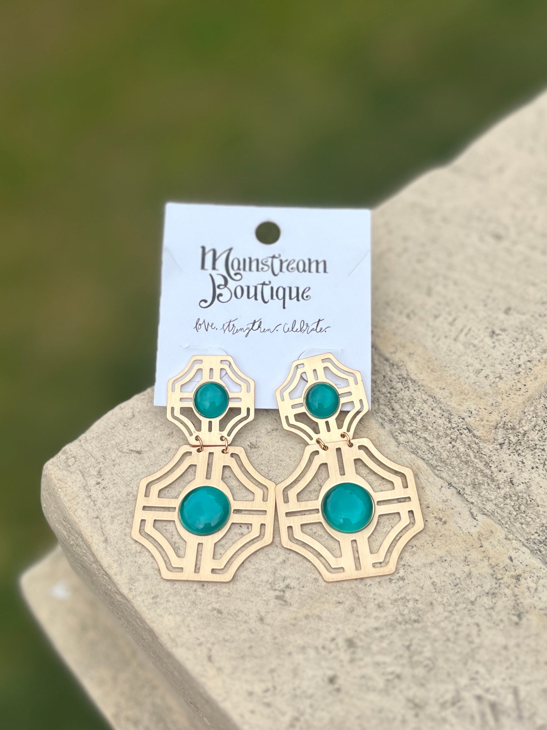 Gold earrings with turquoise stones placed on a stone surface.