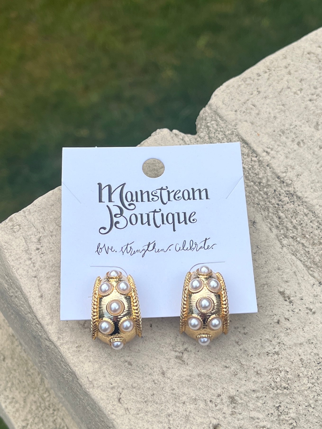Gold and pearl earrings placed on a stone surface.