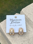Gold and pearl earrings placed on a stone surface.