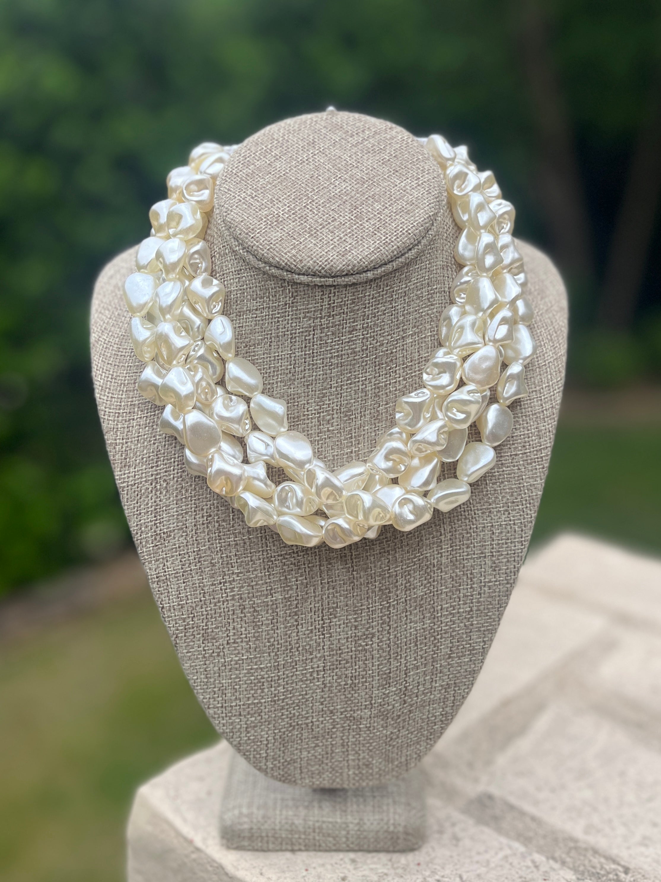 White pearl necklace on a gray bust with a blurred green background
