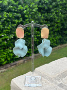 Pair of earrings on a stand with a green outdoor background