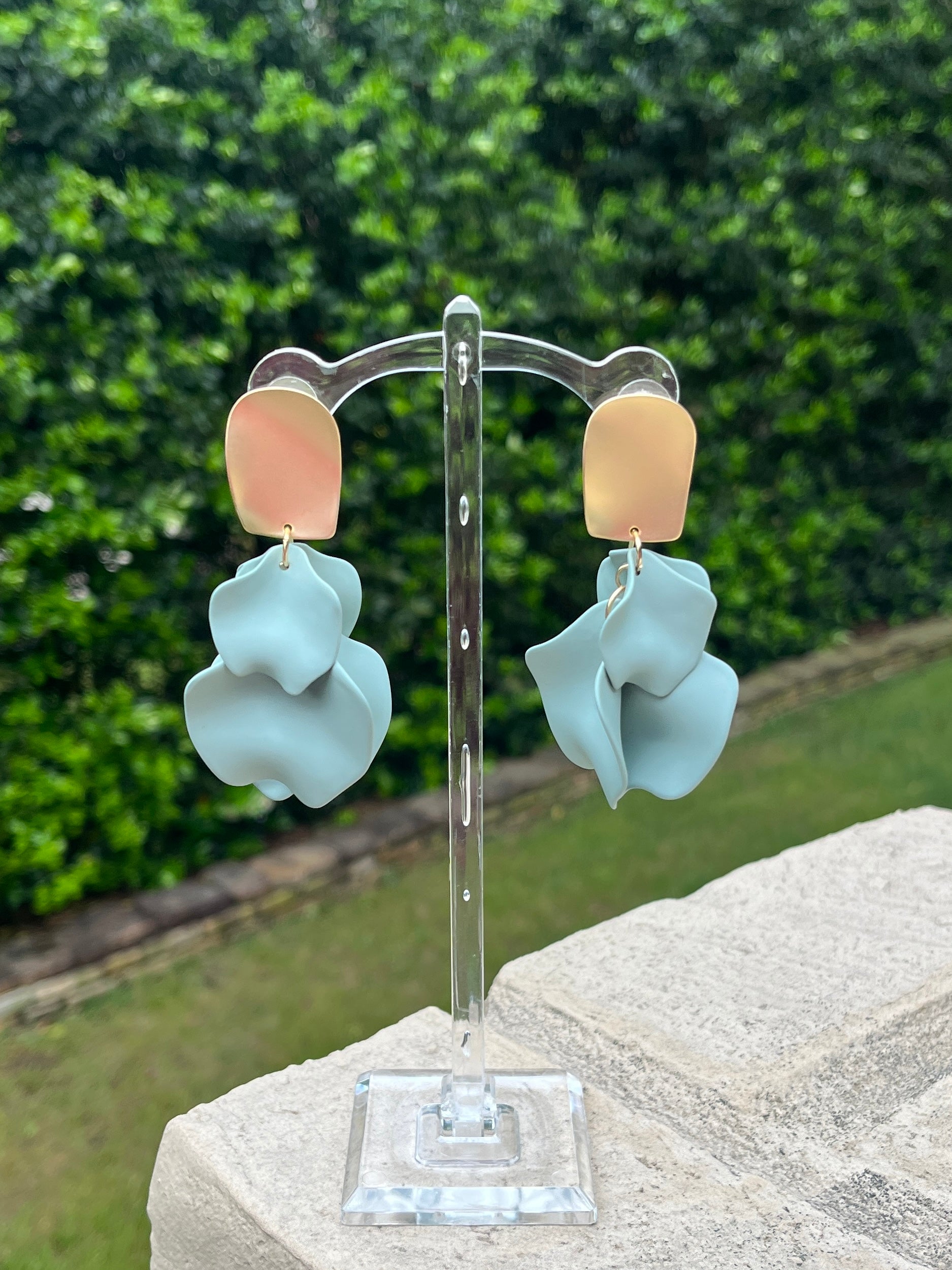 Pair of earrings on a stand with a green outdoor background