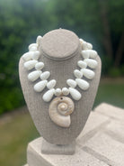 Necklace with white stones and a shell on a gray stand against a blurred green background