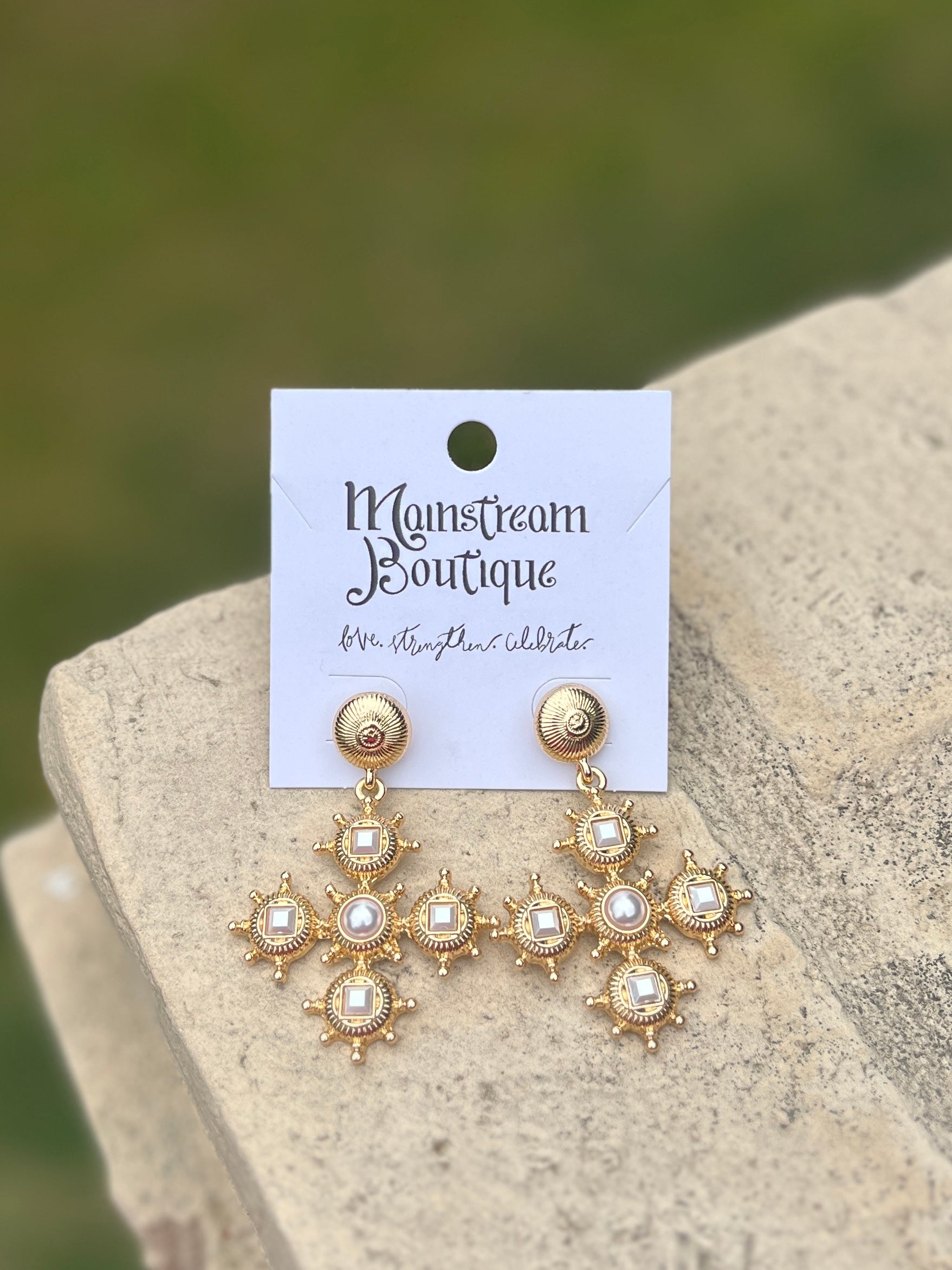 Gold and pearl earrings placed on a stone surface.