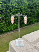 Pair of gold/pearl earrings on a clear stand with a green outdoor background