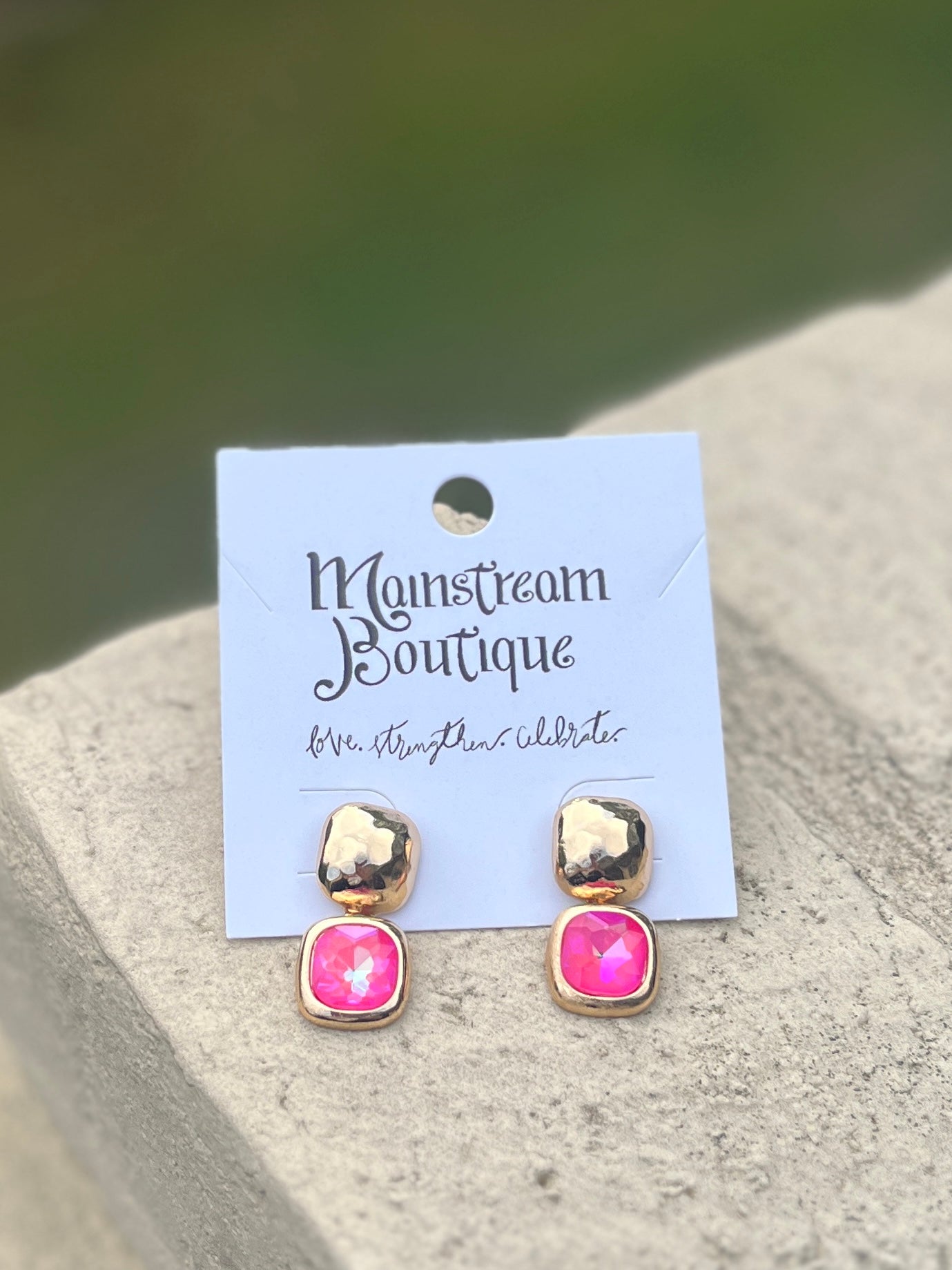 Pair of gold and pink stone earrings against a blurred natural background.
