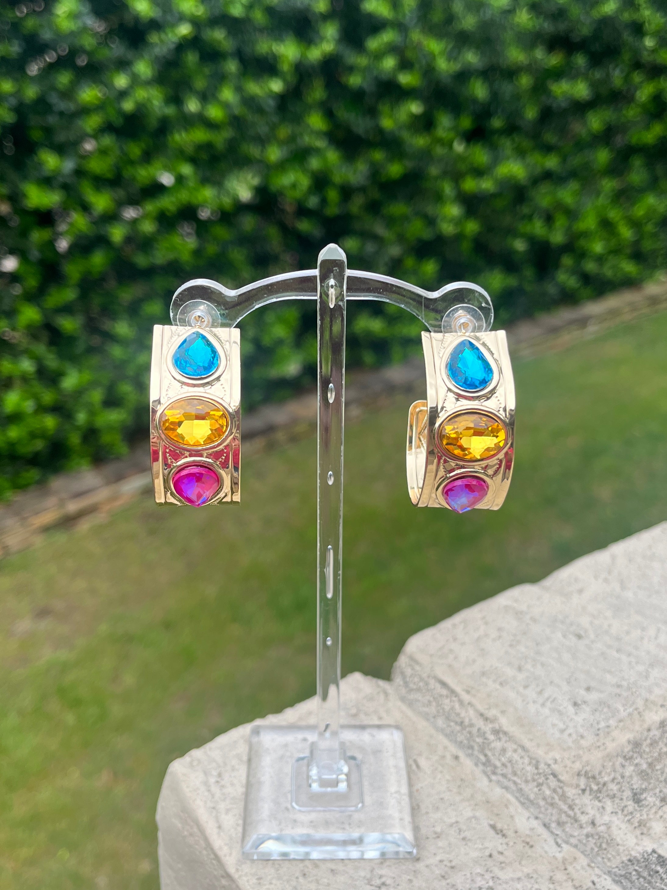 Colorful gemstone earrings on a stand with a green outdoor background