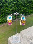 Colorful gemstone earrings on a stand with a green outdoor background