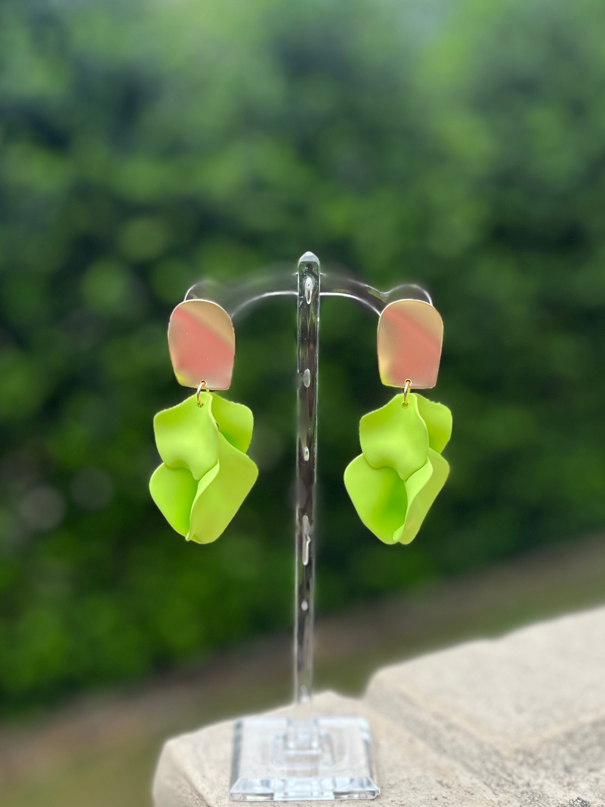 Pair of green flower-shaped earrings on a stand with a blurred green background