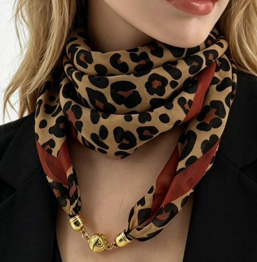 A close-up of a model wearing a leopard print scarf with rust red stripes and gold-toned chain links at the bottom.