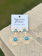 Gold earrings with blue stones placed on a stone surface.
