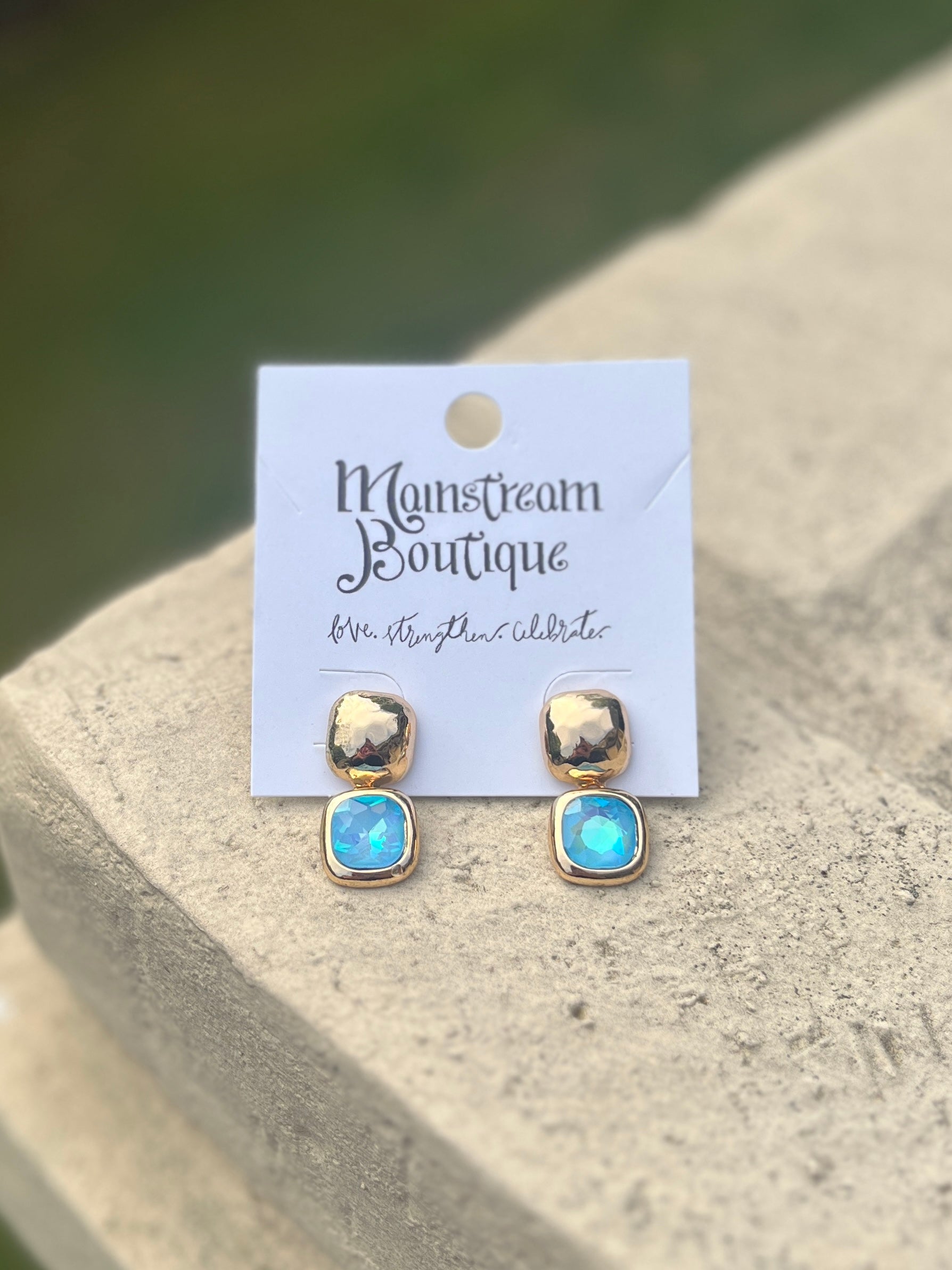 Pair of gold and blue earrings against a stone surface.