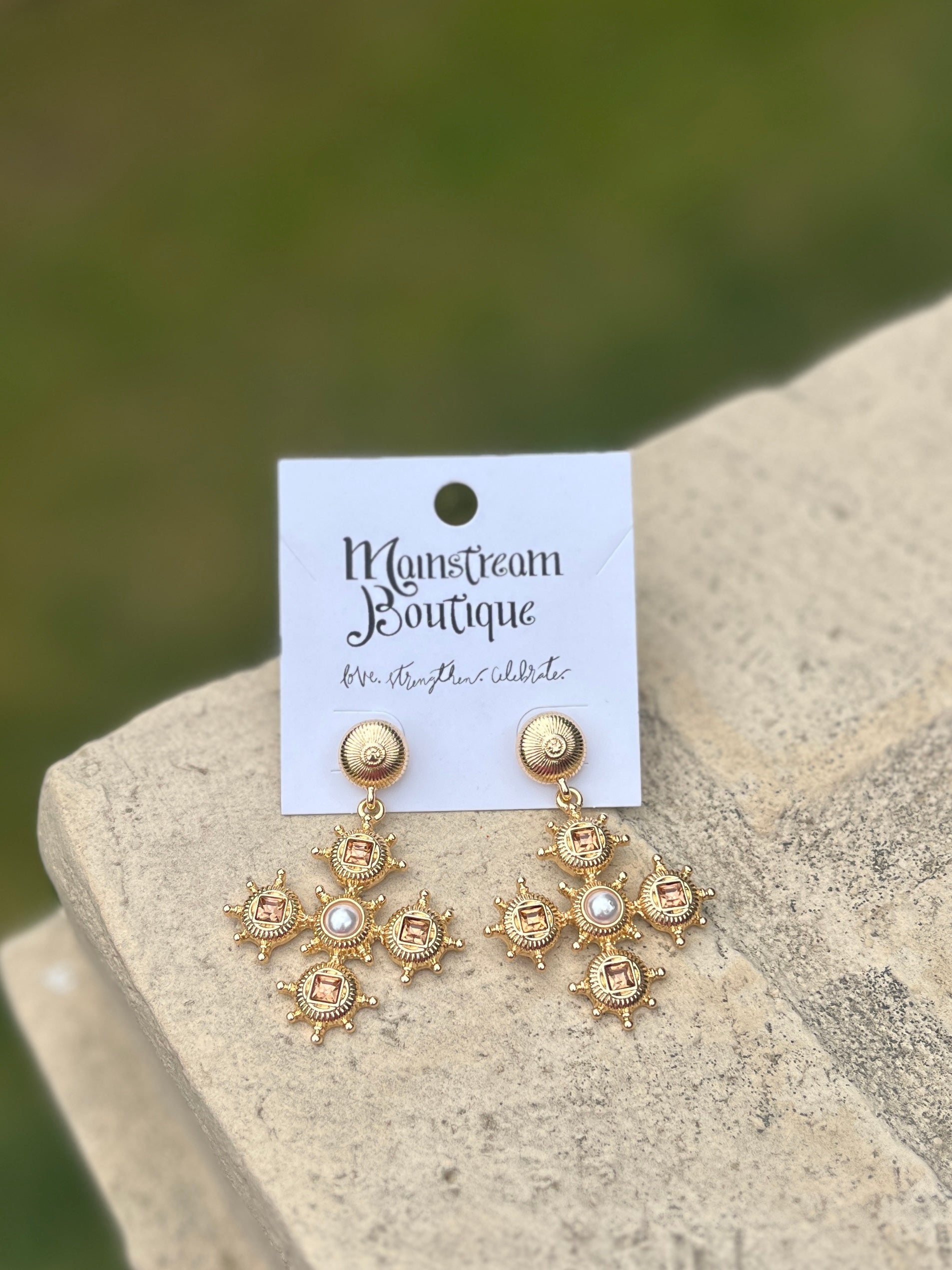 Gold earrings with topaz stones and pearl-like centers on a stone surface.