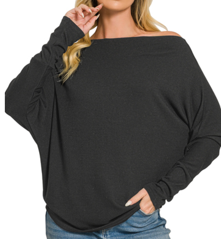 A woman wearing a black off-the-shoulder long-sleeve knit top with a relaxed drape, paired with blue jeans, against a plain white background.