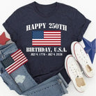 Navy t-shirt with American flag design celebrating the 250th birthday of the USA, paired with denim jeans and white sneakers on a light gray background.