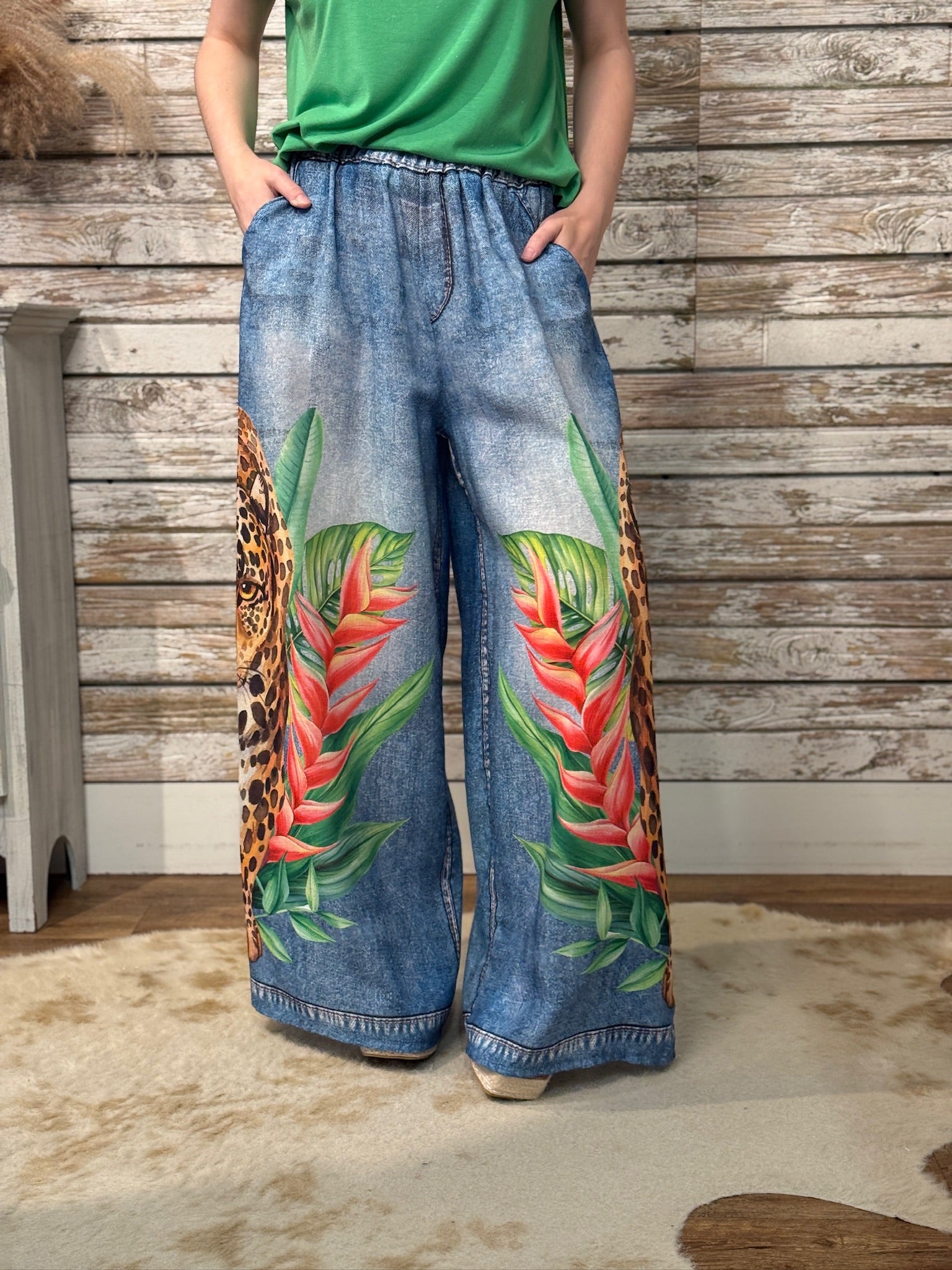 Person wearing blue jeans with tropical leaf design against a wooden wall.