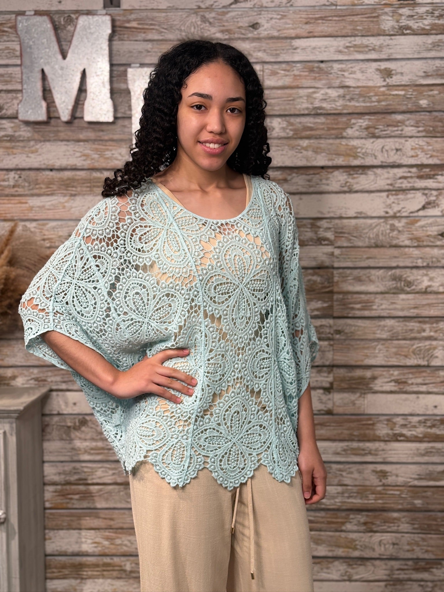 Woman wearing a light blue crochet lace top against a wooden background