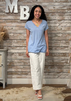 Woman wearing a blue top and white pants standing against a wooden wall with decorative letters.