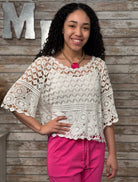 Woman wearing a white crochet top and pink pants against a wooden background