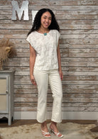Woman wearing a white lace top and pants standing against a wooden paneled wall.