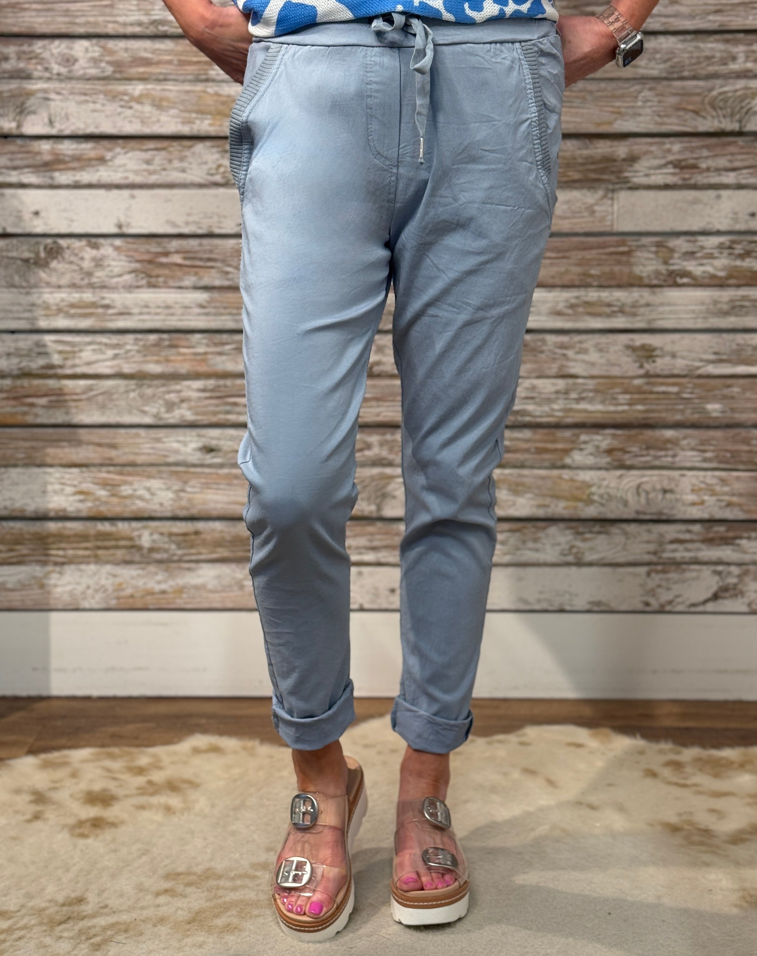 Person wearing light blue jogger pants standing against a wooden wall.