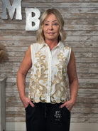 Woman wearing a white blouse with gold embroidery against a wooden wall.
