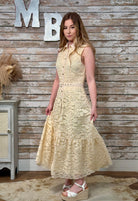 Woman wearing a yellow lace dress standing against a wooden wall with decorative letters.