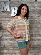 Woman wearing a colorful striped shirt against a wooden wall with large letters.
