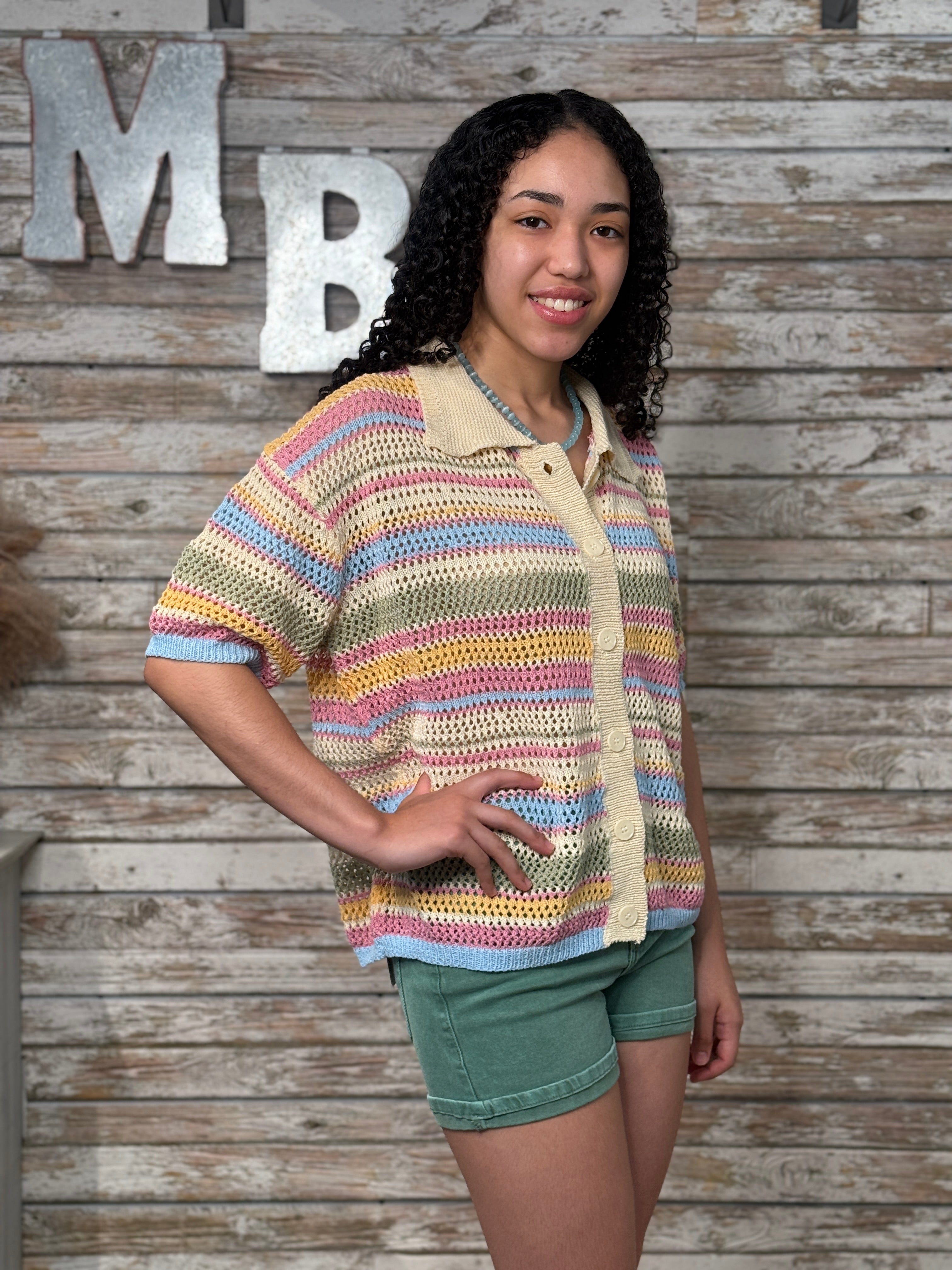Woman wearing a colorful striped shirt against a wooden wall with large letters.