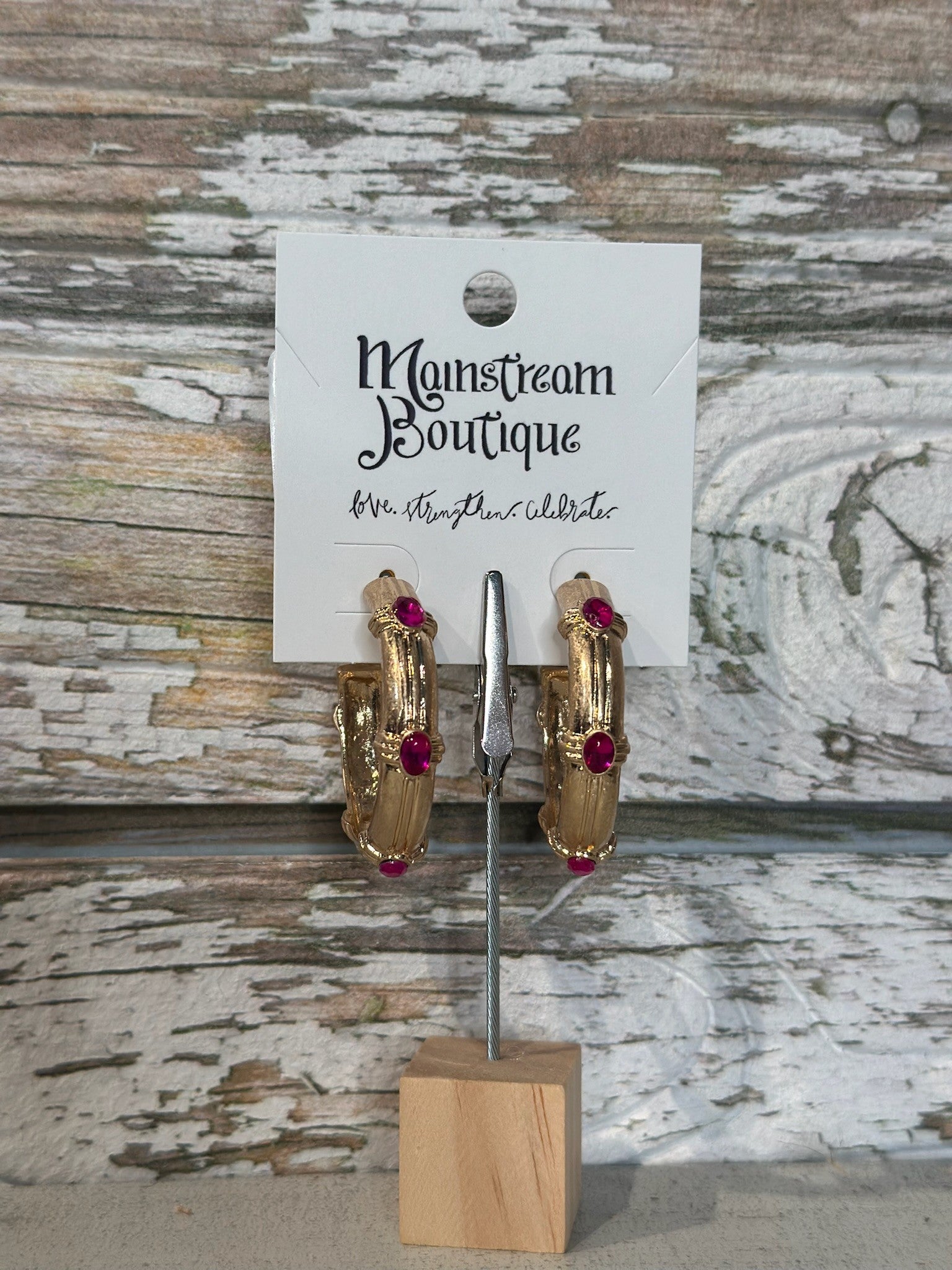 Gold hoop earrings with fuschsia stones on a stand against a rustic wooden background
