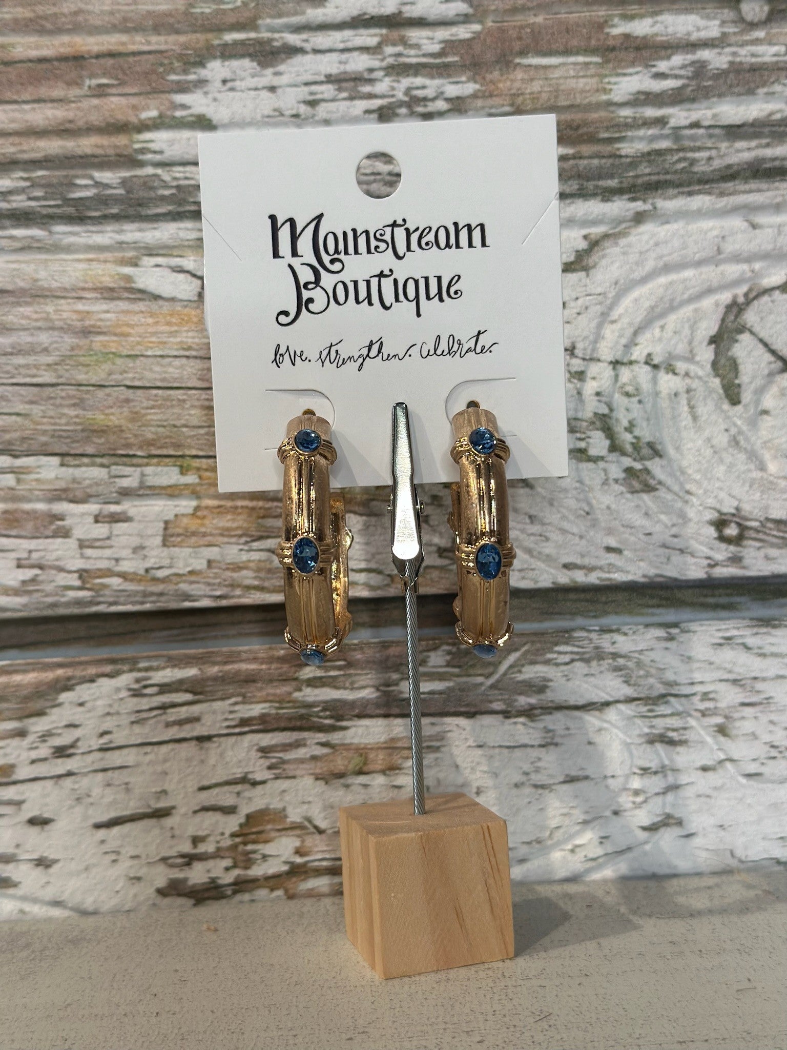 Gold hoop earrings with blue stones on a wooden stand against a rustic wooden background.