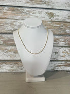 Gold necklace on a white mannequin bust against a rustic wooden background
