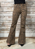 Leopard print flared pants worn by a person against a wooden wall.