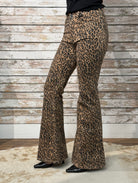 Leopard print bell-bottom pants worn by a person against a wooden wall.