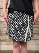 Person wearing a black and white patterned skirt with a wooden background