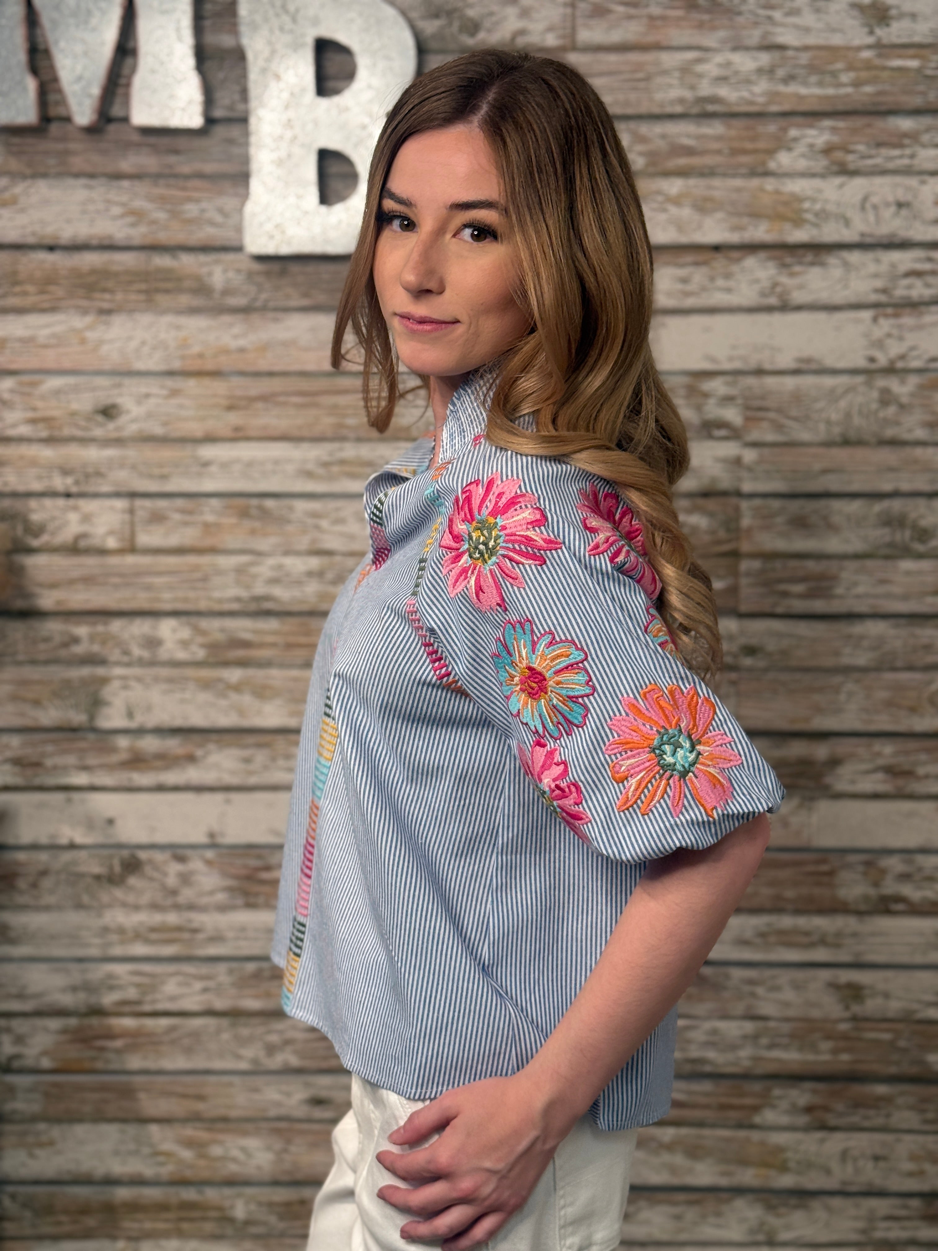 Woman wearing a blue shirt with floral embroidery against a wooden background