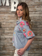 Woman wearing a blue shirt with floral embroidery against a wooden background
