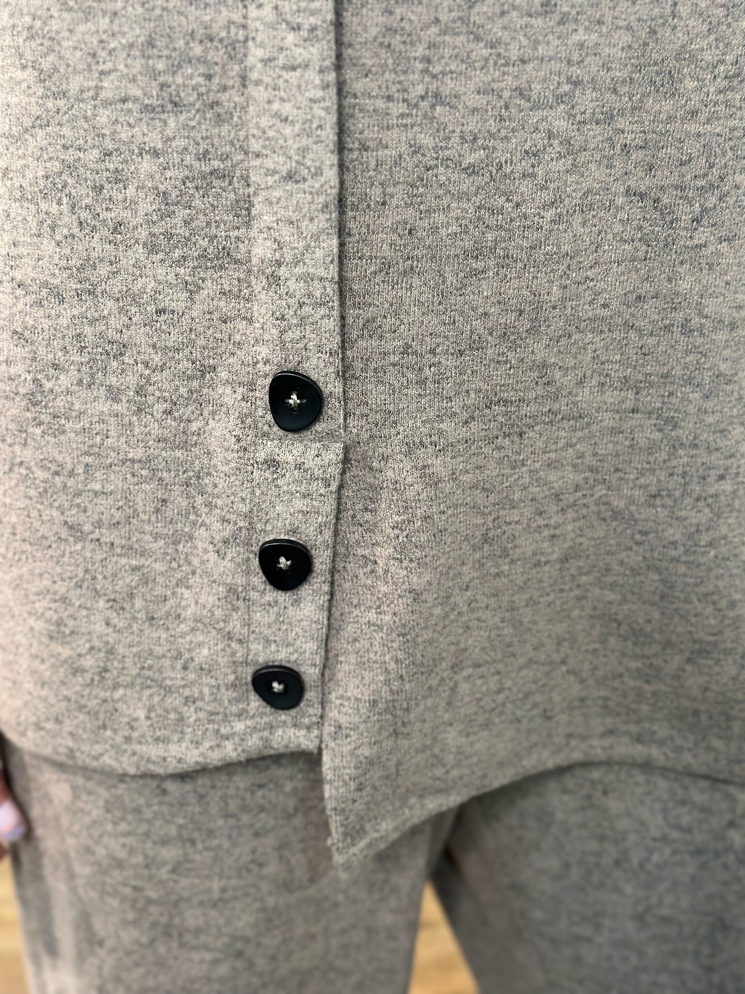 Close-up of a knit garment with three black buttons down the front, showing the fabric texture and button details.
