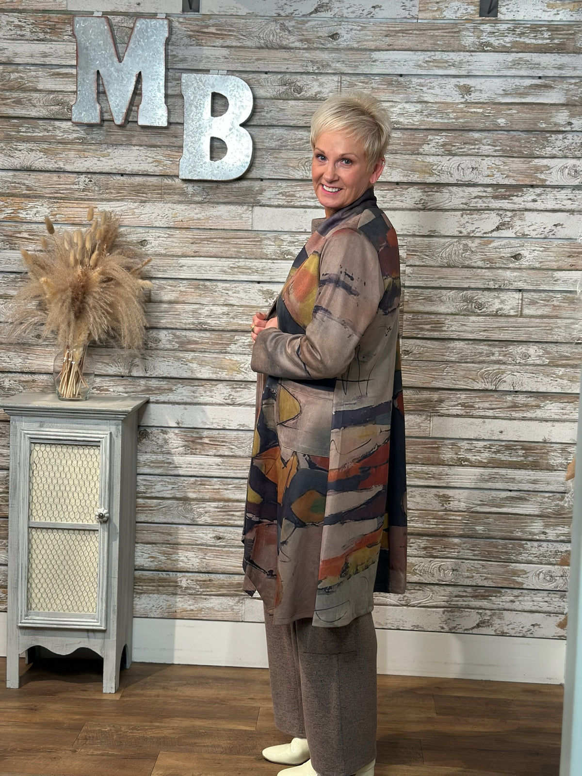 A woman wearing a long-sleeved abstract print cardigan over a brown top and matching pants.
